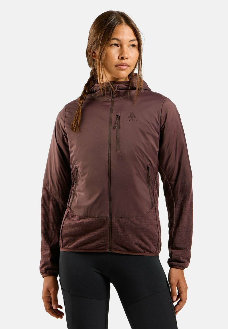 Veste à capuche bordeaux avec des manches texturées, des poches zippées et un logo sur la poitrine. Fabriquée en matériau léger et résistant aux intempéries.