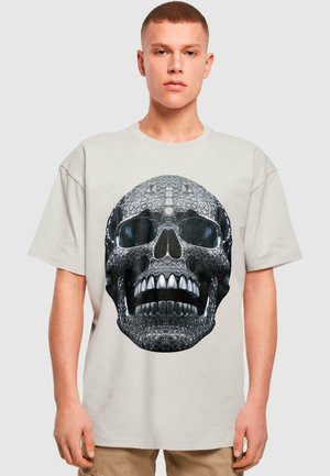 Lichtbeige t-shirt met korte mouwen, voorzien van een grote grafische print van een gedetailleerd schedelontwerp in zwart en zilver met glanzende accenten.