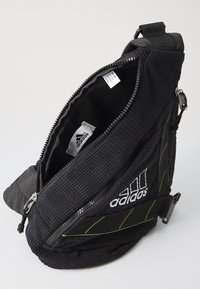 Black polyester crossbody bag with a textured surface, zip closure, green accents, and white logo. Interior lined with smooth fabric.