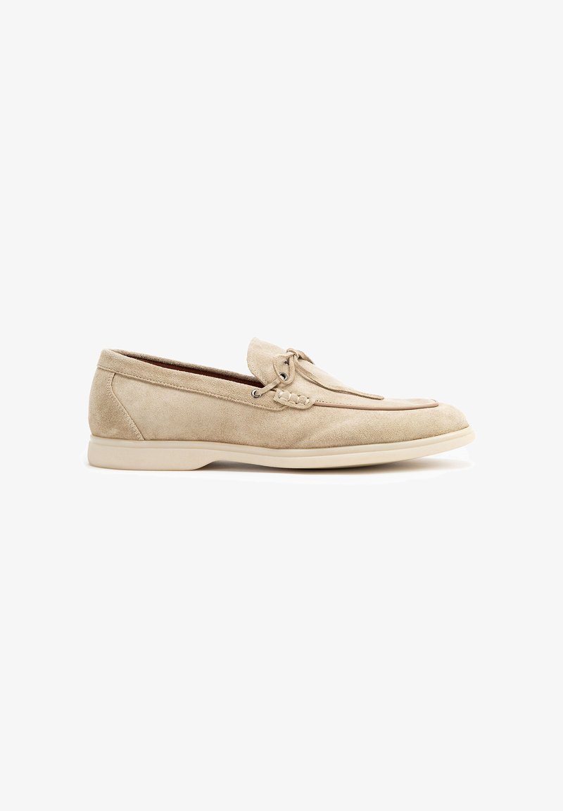 Zapato estilo mocasín de ante beige con una textura suave, acento de cordones y suela de goma crema. Diseño de punta redondeada, detalle de costura sutil.