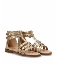 Sandalias metálicas doradas con suela plana, con múltiples tiras horizontales adornadas con tachuelas y dos correas ajustables con hebilla.