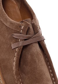 Bruine suède moccasin met zichtbare stiksels en een gestrikte veter over de wreef, met de zachte leren binnenvoering zichtbaar.