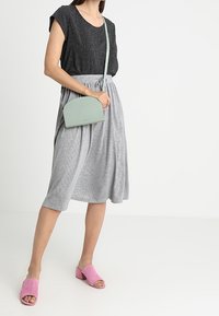 Czarny top z krótkim rękawem, szara midi spódnica w paski, różowe mule na otwartym palcu oraz torebka na pasku w kolorze mięty. Gładka tkanina, luźny krój.