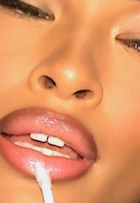 Nahaufnahme von Lippen mit glänzendem, rosa Schimmer; weißer Applikator berührt die Unterlippe; glatte Textur und definierte Form.