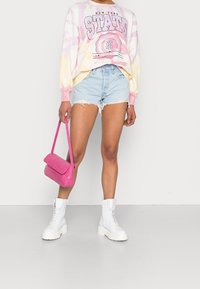 Sudadera de gran tamaño de tie-dye en rosa y amarillo, pantalones cortos de mezclilla clásicos, botas blancas con cordones y un bolso en relieve de cocodrilo rosa.