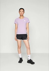 Licht paarse atletische t-shirt met ronde hals, korte mouwen en een subtiel stippenpatroon; gecombineerd met zwarte shorts en zwarte sneakers.