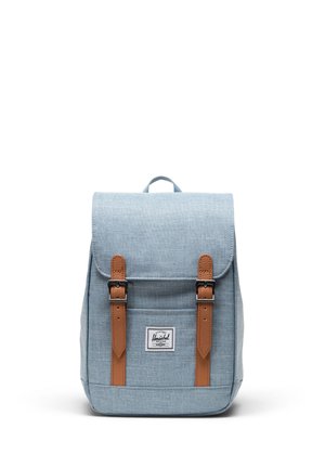 Sac à dos en tissu bleu clair avec deux sangles à boucle marron et une étiquette frontale, présenté debout sur fond blanc.