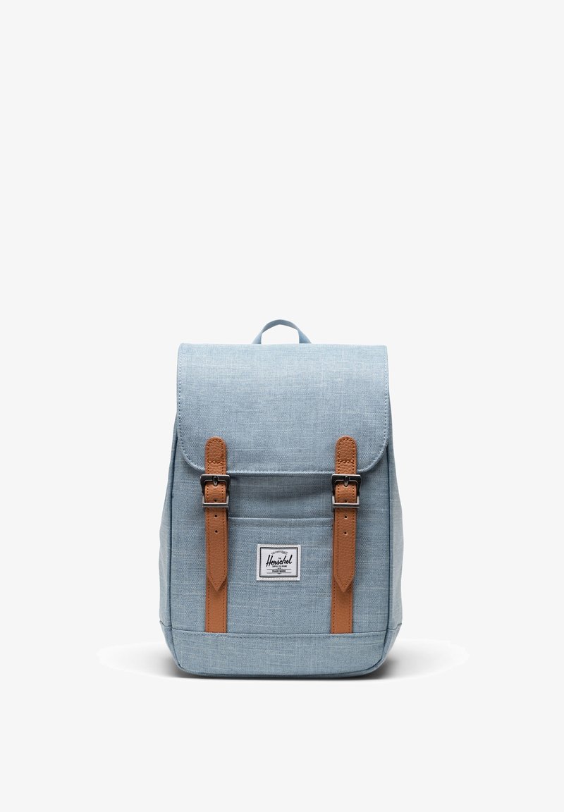 Sac à dos en tissu bleu clair avec deux sangles à boucle marron et une étiquette frontale, présenté debout sur fond blanc.