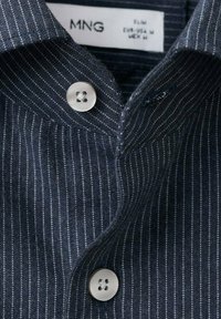 Camiseta con rayas marineras y textura suave, con cuello abotonado y botones de tono plateado. Finas rayas blancas añaden un sutil contraste.