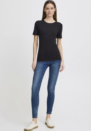 T-shirt en coton noir à manches courtes, assorti à un jean skinny bleu. Le modèle porte des baskets blanches avec une semelle marron clair. Design simple.