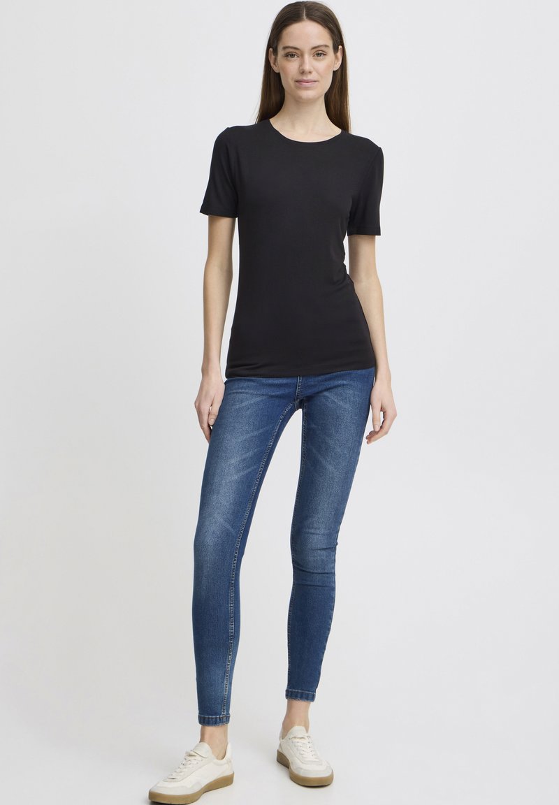 Černé bavlněné tričko s krátkým rukávem, doplněné modrými skinny džíny. Model má na sobě bílé tenisky se světle hnědou podrážkou. Jednoduchý design.