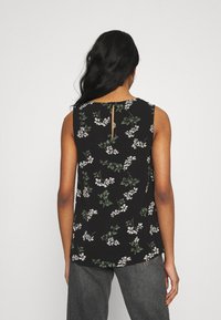 Mouwloos zwart bloemen top met witte en groene patronen. Voorzien van een keyhole sluiting op de rug en een ontspannen pasvorm. Glad stoftextuur.