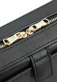 Borsa in pelle nera con superficie texture, dotata di zip e tirante in tonalità oro, cuciture dettagliate e forma rettangolare.