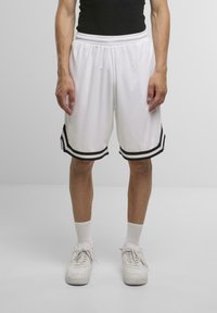 Hvide basketballshorts med sorte striber i kanten, elastisk talje og løs pasform, parret med hvide sneakers og sokker.