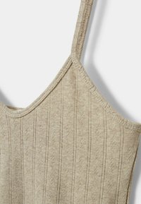 Bežani pleteni top s tankim naramenicama. Rebrasta tekstura s okomitim uzorcima. Meki, lagani materijal prikladan za tople vremenske uvjete.