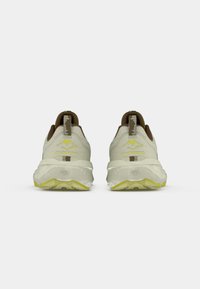 Weiße Laufschuhe mit einer strukturierten Sohle, braunen Akzenten und einer reflektierenden Fersenschlaufe. Sie verfügen über eine gepolsterte Zwischensohle und eine gemusterte Außensohle.