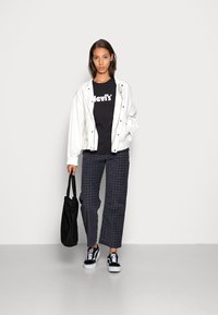 Chaqueta bomber blanca, camiseta negra de Levi's, pantalones de cuadro en azul marino y blanco. Bolsa de mano negra y zapatillas negras con suelas blancas.