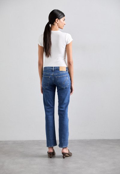 Jeans de mezclilla azul con un ajuste clásico, cintura media y dos bolsillos traseros, combinados con una blusa blanca ajustada de manga corta.