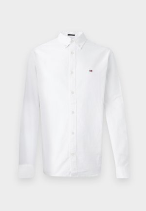 Λευκό πουκάμισο με γιακά, μακριά μανίκια και ένα μικρό κόκκινο, λευκό και μπλε λογότυπο στο αριστερό στήθος. Φτιαγμένο από βαμβακερό ύφασμα.