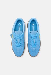 Blå mockasneakers med låg profil och texturerade detaljer, med platta snörningar och en brun gummisula. "Ortholite"-varumärke inuti.