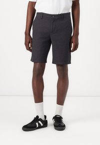 Grå shorts lavet af tekstureret stof, med knaplukning, bæltestropper og sidelommer, parret med sorte sneakers og hvide sokker.