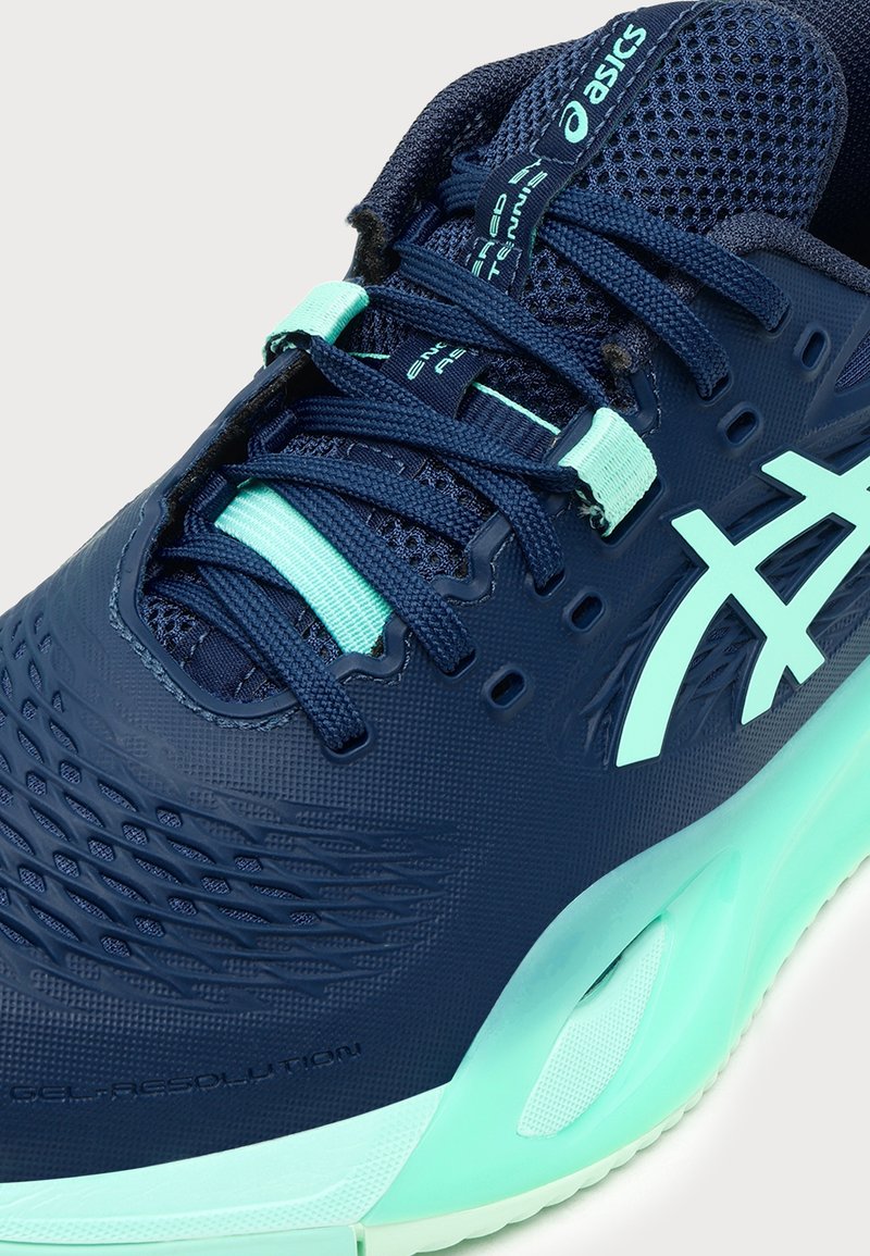 Chaussure de course Asics bleu marine et vert menthe avec empeigne en mesh, lacets détaillés et logo signature sur le côté, vue en gros plan.