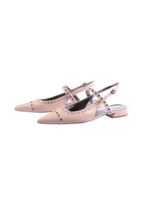 Beige Lackleder-Ballerinas mit spitz zulaufender Form, Ankle-Straps und silbernen Ösen-Detaillierungen, vor einem weißen Hintergrund.