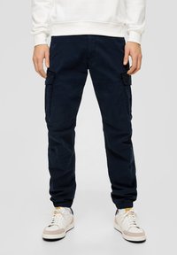 Marine cargo broeken met een comfortabele pasvorm, voorzien van zijzakken en elastische boorden. Gedragen met witte sneakers en een lichte sweatshirt.