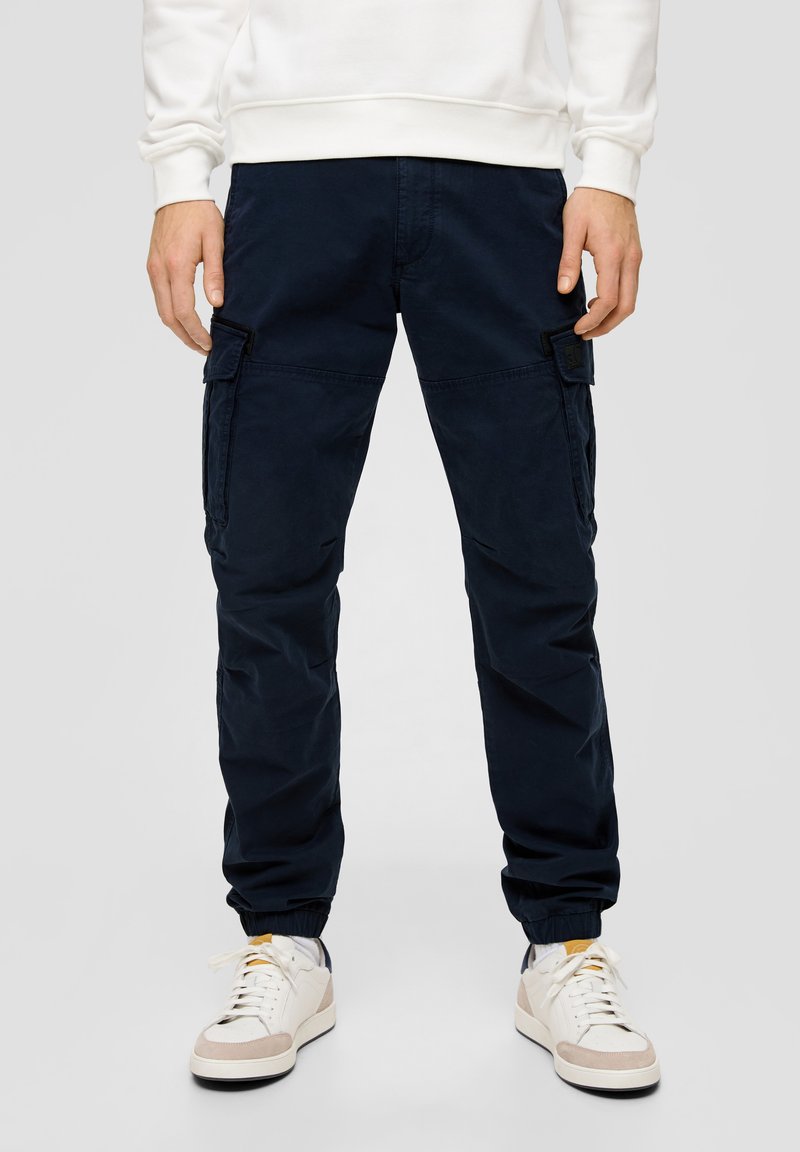 Marine cargo broeken met een comfortabele pasvorm, voorzien van zijzakken en elastische boorden. Gedragen met witte sneakers en een lichte sweatshirt.