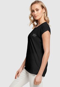 T-shirt en coton noir à manches courtes, avec un texte blanc qui dit "Soyez doux mais restez en sécurité." Coupe décontractée et texture douce.