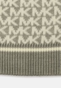 Close-up of green and white knitted fabric with geometric zigzag and star patterns above a ribbed hem.