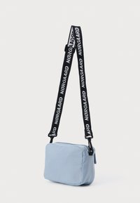 Jasny niebieski prostokątny plecak na ramię wykonany z miękkiego materiału, z czarnym paskiem, na którym wielokrotnie nadrukowano nazwę "Nørgaard" w białym kolorze.