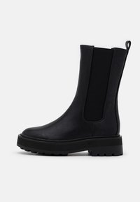 Botas Chelsea negras con parte superior de cuero liso, paneles laterales elásticos y suela de goma resistente. Presentan una puntera redondeada y diseño sin cordones.