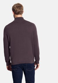 Dunkelvioletter Pullover mit hohem Kragen, gerippten Bündchen und Saum, kombiniert mit blauen Jeans. Weiche Textur und taillierte Passform.