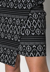 Sort og grå mønstret kjole med geometriske design, med en tætsiddende silhuet og en delt kant for ekstra detalje.