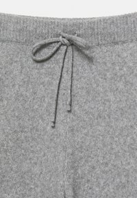 Grå strikkede bukser med elastisk talje og snor. Teksturen er blød med et let mønster, og kanten har et diskret split-design.