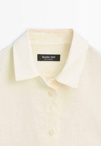 Crèmekleurig overhemd met kraag en knoopsluiting, met een zwart label met de tekst "Massimo Dutti Made in Morocco" aan de binnenkant van de halslijn.