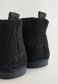 Botine negre pufoase până la gleznă, cu un material superior texturat, featuring un material moale asemănător cu blana de oaie și tălpi din cauciuc plate, concepute pentru confort.