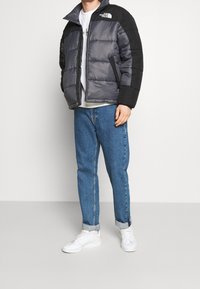 Foret jakke i grå og sort med lynlås hele vejen foran, sidelommer og høj krave. Kombination med lyseblå jeans og hvide sneakers.