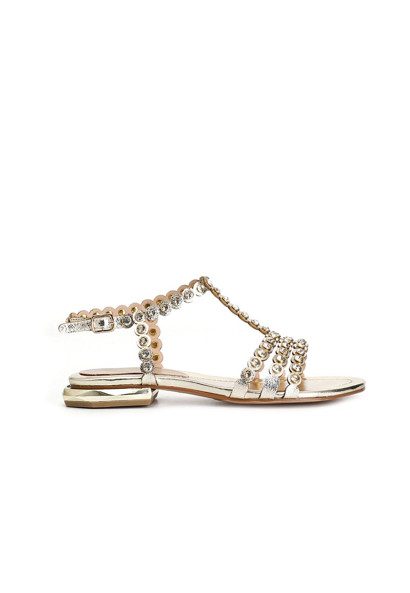 Guldtonad sandal med platt klack, prydd med cirkulära dekorationer och rhinestones på remmarna. Slät textur, öppen design.