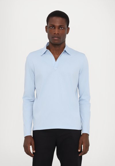 Cămașă polo albastru deschis, cu mânecă lungă și guler ascuțit, cu o clapetă cu jumătate de buton. Material moale, cu o textură netedă. Pantaloni negri.