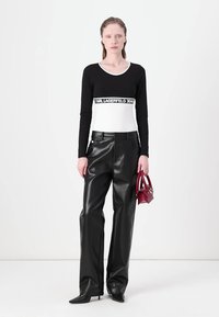 Black long-sleeve top with white bottom and logo band, paired with high-waisted black faux leather trousers and a small burgundy handbag.