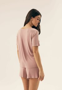 Różowy zestaw odzieży do relaksu składający się z luźnej bluzki z krótkim rękawem i dopasowanych szortów; miękka tkanina o gładkiej fakturze i minimalnych detalach szwów.
