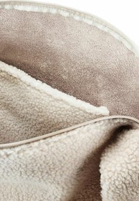 Tessuto in pile color crema con una consistenza morbida e strutturata, caratterizzato da una fodera marrone liscia e un bordo con zip metallica.