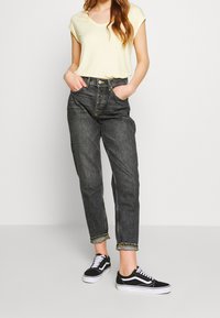 Žlutá a bílá pruhovaná košile s krátkým rukávem v kombinaci s džíny s vysokým pasem v tmavém denimovém provedení. Model má na sobě černé tenisky s bílými podrážkami.