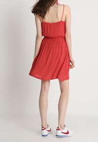 Robe rouge sans manches avec une taille élastique, jupe évasée et tissu léger. Associée à des baskets blanches avec des accents rouges.