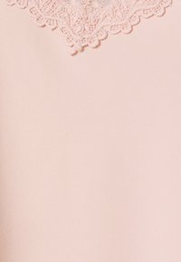 Tessuto rosa chiaro con superficie testurizzata e delicati dettagli in pizzo sul bordo superiore. Il pizzo presenta motivi intricati e bordi smerlati.