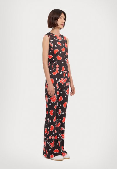 Black jumpsuit featuring large red hearts and floral patterns, sleeveless design, and flared legs, paired with white shoes.
