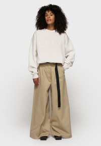 Felpa over-size crema con testo "10DAYS", abbinata a pantaloni beige a gamba larga con dettaglio di cintura nera. Scarpe nere con plateau.