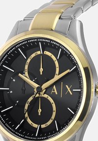 Ura iz nerjavečega jekla z zlatim in srebrnim pasom. Črno številčnico odlikujejo zlati poudarki, tri subštevilčnice in beli označevalci za ure.